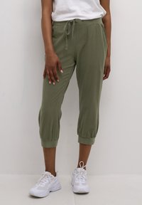 Gröna korta joggerbyxor i mjukt tyg med elastisk midja och dragsko samt mudd runt anklarna. Matchas med vita sneakers.