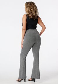 Pantalons évasés gris en tissu doux et extensible. Design taille haute avec de subtils détails de couture. Portés avec un haut sans manches noir.