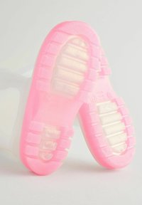 Semelles de sneakers transparentes avec une base en caoutchouc rose épais, dotées de rainures texturées et d'une finition brillante, adaptées à un style décontracté.