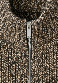 Sweter z dzianiny z wysokim kołnierzem w brązowo-kremowej kolorystyce, z metalowym zamkiem błyskawicznym na przodzie i fakturowanym wzorem tkaniny.