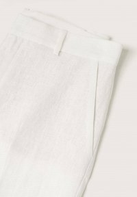 Pantalon en lin blanc avec une texture lisse, un devant plissé et une ceinture plate. Le tissu présente une apparence subtile et légère.