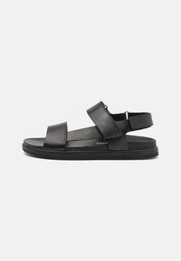 Black leather sandals feature two wide straps across the foot, adjustable heel strap, and a textured rubber sole for grip.