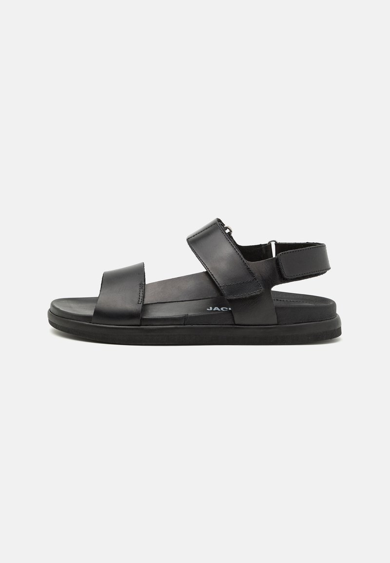 Black leather sandals feature two wide straps across the foot, adjustable heel strap, and a textured rubber sole for grip.