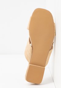 Sandale en paille tressée avec bout carré, semelle plate et petit talon bloc, vue par dessous sur fond blanc.
