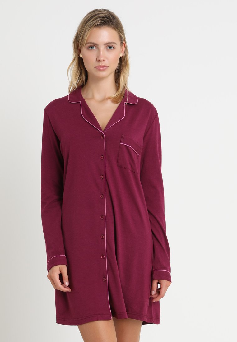 Long-sleeve, burgundy nightdress made of soft fabric. Features button front, pocket, and contrasting pink piping along the collar and cuffs.