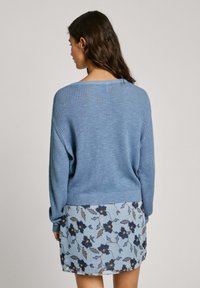 Gaiši zils ribots džemperis ar brīvu piegriezumu, ar apaļu kakla izgriezumu un garām piedurknēm, kombinēts ar ziedu raksta svārkiem.