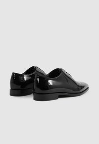 Scarpe eleganti nere lucide con punta affilata, texture liscia, tacco piatto e sistema di allacciatura; dettagli di cucitura sottili migliorano il design.