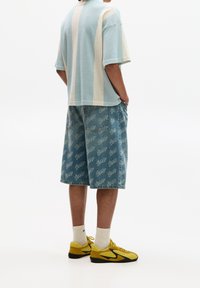 Světle modré pletené tričko s krátkými rukávy a bílými pruhy, v kombinaci s džínovými šortkami se vzorem opakujícího se loga a žlutými teniskami.