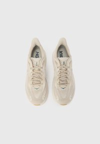 Μπεζ αθλητικά παπούτσια με επάνω μέρος από δίχτυ, στρογγυλή μύτη και δέσιμο με κορδόνια. Υφασμάτινες λεπτομέρειες και διακριτική σήμανση λογότυπου στη γλώσσα.