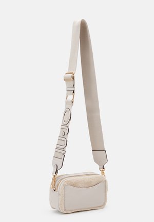 Sac bandoulière beige avec poche avant en tissu pelucheux, fermetures éclair dorées et large sangle beige réglable avec texte décoratif bordé de noir.