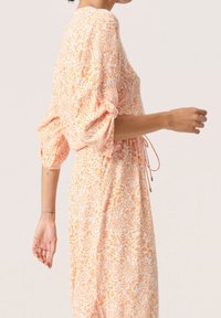 Šaty s květinovým vzorem v oranžové a bílé barvě, volný střih, nabírané rukávy, stahovaný pas a texturovaná látka.