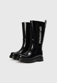 Bottes de pluie en caoutchouc noir avec une finition brillante, semelle robuste et texte imprimé en blanc détaillant la marque "KARL LAGERFELD" et le lieu.