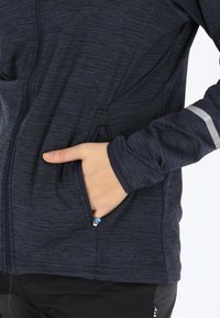 Navy blue zip-up jacket made of textured material featuring side pockets and a reflective stripe on the sleeve.