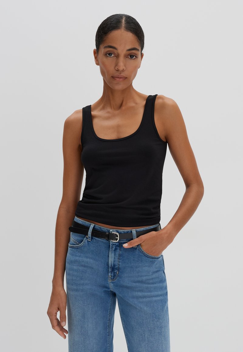 Schwarzes Baumwoll-Tanktop mit breiten Trägern, Rundhalsausschnitt und taillierter Silhouette, kombiniert mit blauen Jeans und einem schwarzen Gürtel.