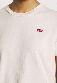 Ljusrosa t-shirt av bomull med rundad halsringning och korta ärmar, prydd med en liten röd Levi's-logotyp på vänster bröst.