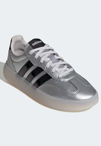 Silverfärgad träningssko med svarta ränder, slät syntetisk ovandel, snörning, vadderad krage och genomskinlig gummisula.