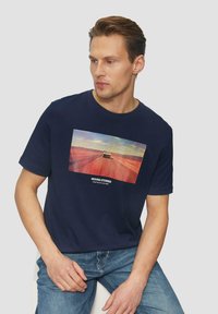 Marineblauw katoenen T-shirt met een graphic op de voorkant van een auto op een weg met een zonsondergang op de achtergrond. Ronde hals en korte mouwen.