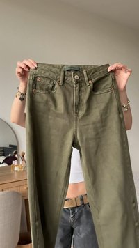 Oliivinvihreät puuvillahousut, joissa etutaskut, näkyvät saumat ja kuparisävyiset napin koristeet, esillä neutraalia taustaa vasten.