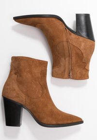 Brune ruskinds-ankelstøvler med spids tå og buet sidedetalje, med en sort stablet hæl og lynlås i siden til lukning.