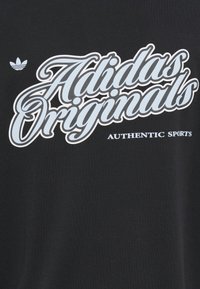 Μαύρο μπλουζάκι με μεγάλο λευκό και γαλάζιο κείμενο "Adidas Originals" και τη φράση "AUTHENTIC SPORTS" από κάτω, με το λογότυπο τριφύλλι της Adidas.
