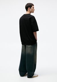 Tricou oversized negru cu mâneci scurte, asociat cu blugi decolorati, largi. Purtați cu adidași albi, design minimalist.