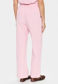Light pink wide-leg pants with an elastic waistband. Fabric has a smooth texture. Paired with brown ballet flats.