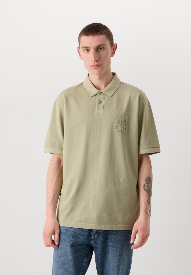 Polo-shirt vert clair en coton, avec un col à deux boutons et un logo "HUGO" brodé sur la poitrine gauche. Manches courtes.