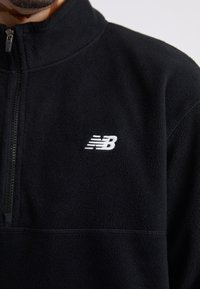 Juodas vilnos džemperis su aukštu apykakle ir užtrauktuku. Ant krūtinės dalies yra mažas baltas "New Balance" logotipas. Malonus prisilietimas.
