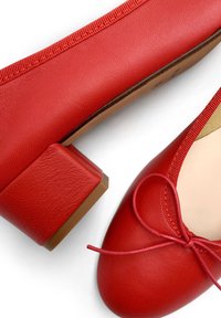 Bailarinas de cuero rojo con punta redonda, ribete elástico y un pequeño tacón cuadrado. El zapato presenta un lazo atado en la parte frontal.