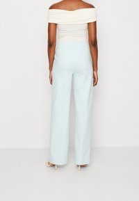Lichtblauwe wijde broek met een gladde textuur, hoge taille en strakke lijnen, gedragen met een aansluitend off-white top.