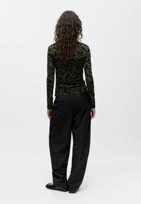 Long-sleeve top with dark green sheer fabric and black floral pattern; paired with loose black trousers and shiny black shoes.