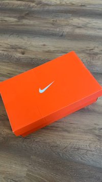 Boîte à chaussures Nike orange avec un logo swoosh Nike bleu sur le dessus. Forme rectangulaire avec une surface lisse et plate.