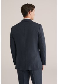 Giacca da abito blu scuro su misura, tessuto strutturato, spacco singolo sul retro, dettagli in bottoni sulle maniche, con pantaloni coordinati.