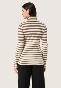 Pulover cu guler înalt, în dungi maro și crem, cu mâneci lungi, design ajustat și textură ribbed, asortat cu pantaloni negri moderni.