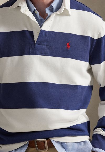 Chemise de rugby rayée bleu marine et blanche avec col à revers, arborant un petit logo de joueur de polo rouge et une coupe décontractée. Matière en coton.
