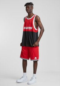 Rød og svart basketballtrøye med hvite detaljer og "STARTER"-logo, sammen med røde shorts med svarte aksenter. Hvite joggesko og sokker.