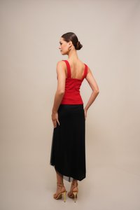 Rood nauwsluitend topje met brede bandjes en een lage rug, gecombineerd met een zwarte rok met een transparant paneel en een licht zwierig zoom. Gele sandalen met hoge hakken.