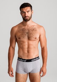 Harmaat boxerit mustalla vyötärönauhalla, jossa on brändinimi "ombre". Materiaali näyttää pehmeältä; muotoilu on tiukka ja pinnassa on sileä rakenne.
