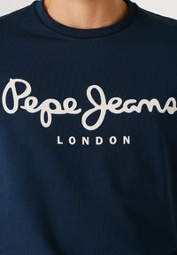 Temno modra majica s kratkimi rokavi z belim napisom »Pepe Jeans London« čez prsni koš.
