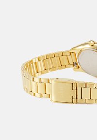 Gouden metalen polshorloge met een brede schakelarmband en een sluiting. Ronde kast met een gladde oppervlakte en gegraveerde merknaam op de achterkant.