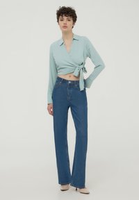 Top avvolgente verde menta con maniche lunghe e un nodo in vita, abbinato a jeans a zampa d'elefante blu denim a vita alta.