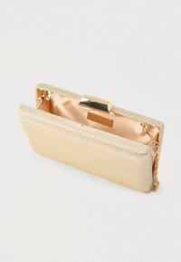 Kabelka v zlatej farbe s textúrovaným kovovým povrchom, saténovým vnútrom a hladkou obdĺžnikovou prackou. Súčasťou je odnímateľný retiazkový popruh.