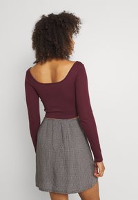 Burgundin värinen ribattu pitkähihainen crop-top, joka on yhdistetty musta-valkoiseen ruutukuvioituun trumpettihameeseen. Sileä rakenne, yksinkertainen pyöreä pääntie.