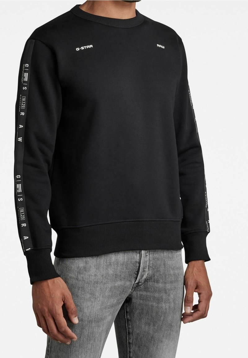 Sudadera negra de mezcla de algodón con cuello redondo acanalado. Presenta un diseño de marca en texto blanco en las mangas y el pecho. Diseño ajustado, mangas largas.