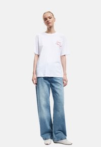 Hvid bomulds t-shirt med korte ærmer, prydet med et pink sløjfe grafik på brystet. Sammen med lyseblå, vide denimbukser.