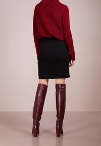 Burgundský žebrovaný svetr v kombinaci s černou přiléhavou sukní a bordó koženými vysokými botami. Hladká textura, štíhlý silueta a design na podpatku.