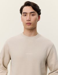 Beige sweatshirt laget av myk, teksturert stoff; har rund hals og en liten brodert "LES DEUX"-logo på brystet.