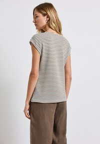 Randig topp i bomull med rundad halsringning och korta ärmar, med växelvis ljusa och mörka horisontella ränder. Matchas med linbuxor.