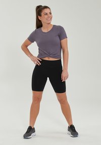 Lila kortärmad t-shirt med knuten fram, tillsammans med högmidjade svarta cykelbyxor och svarta sportskor med vita detaljer.