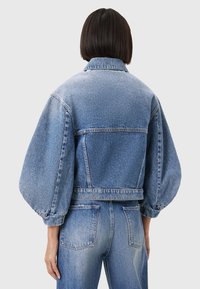 Giacca in denim blu con design cropped, maniche a sbuffo e cuciture in vista. Presenta un colletto classico e tasche posteriori.